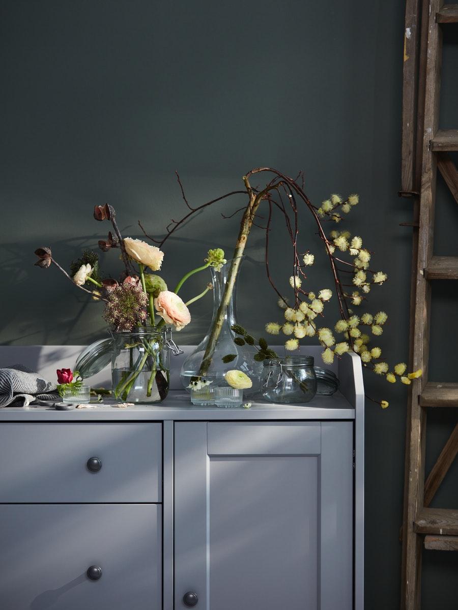 Carafe used as an artifical flower display sat on top of a large grey traditional side table