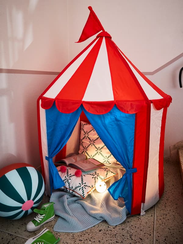 Carpa para niños con temática de circo con cojines, luces y un libro en su interior.