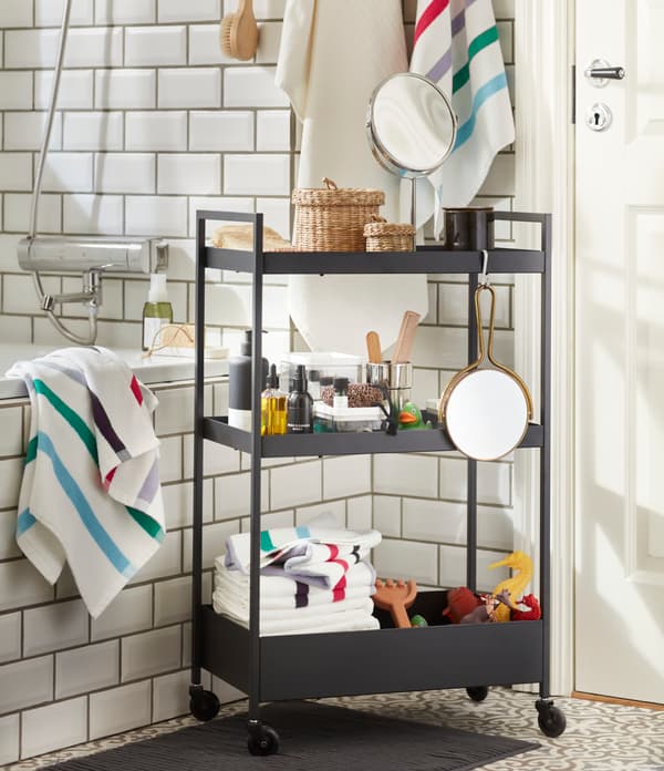 Carrito negro NISSAFORS en un baño, con accesorios de limpieza personal, toallas, espejos y otros artículos.