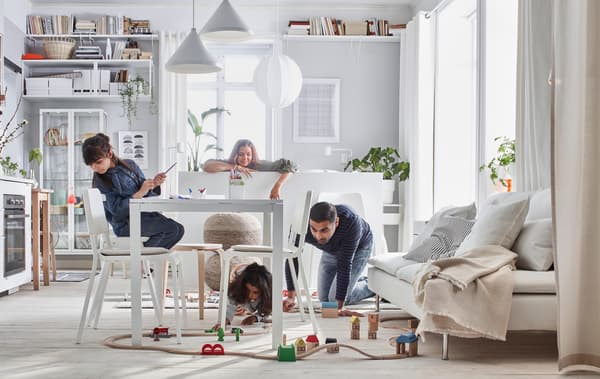 Casa compacta onde uma família brinca com um conjunto de comboio LILLABO numa sala com cama, sofá, mesa, kitchenette e arrumação.