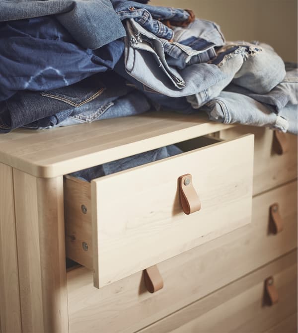 Cassettiera BJÖRKSNÄS in legno con maniglie in pelle. Sopra, alcuni indumenti impilati.
