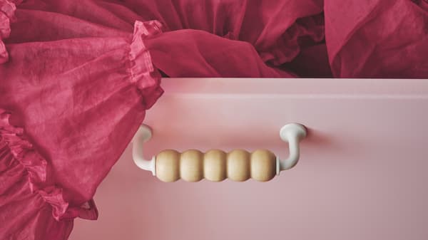 Cassettiera SMÅSTAD con una gonna in tulle che fuoriesce da un cassetto con frontale in rosa chiaro e un’originale maniglia in legno.