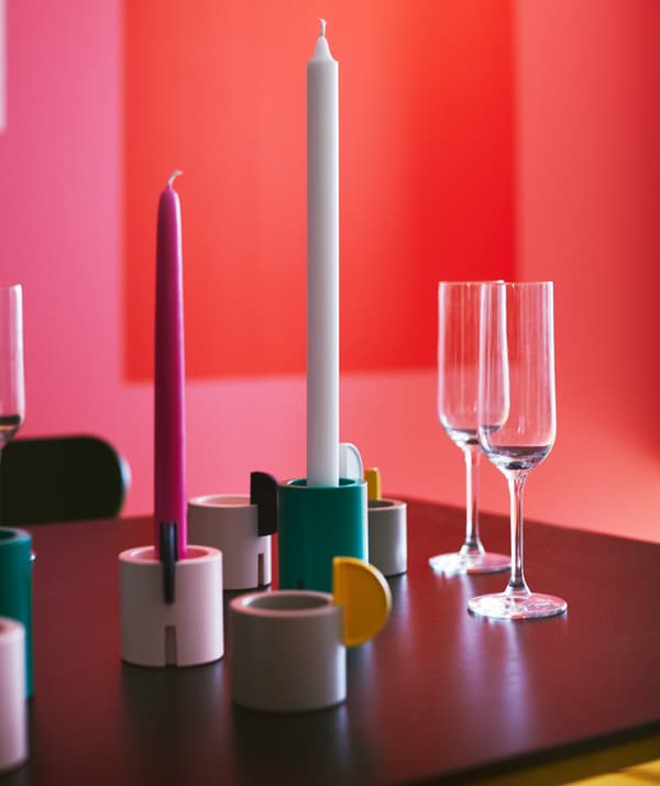 Câteva sfeșnice ÄDELHET sau suporturi pentru lumânări pastilă gri, albe și verzi, cu lumânări în interior, așezate pe masă. 