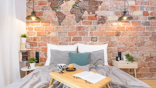 Ceglana ściana, na tle której stoi łóżko.