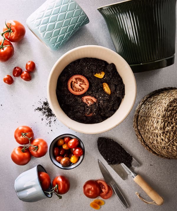 Ceramic and rattan plant pots surrounded by ripe tomatoes. One of the pots is filled with fresh soil and tomato slices.