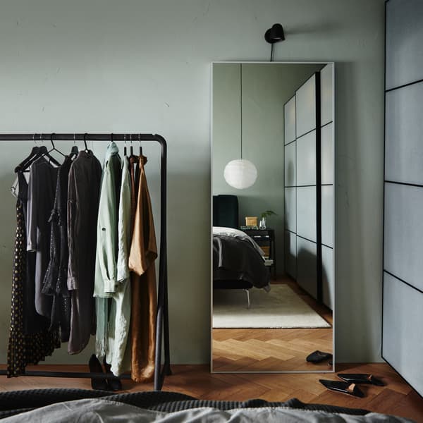 Cermin besar bersandar pada dinding, pakaian tergantung pada rak pakaian, almari pakaian dengan kesan kertas berwarna putih/hitam coklat dan kasut hitam.