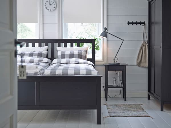 Černohnědý rám postele HEMNES, na ní kostičkované povlečení v bílé a béžové.