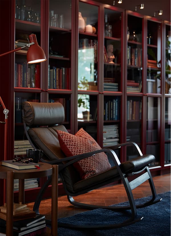 Chaise berçante PÖANG en cuir brun foncé devant quelques bibliothèques BILLY rouge foncé