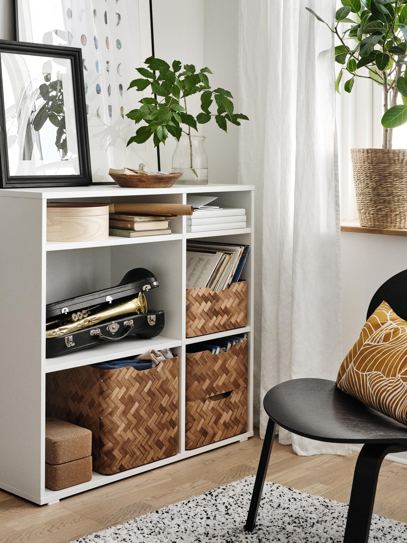 Chaise FRÖSET noire sur laquelle se trouve un coussin jaune foncé, à côté d’une étagère ouverte accueillant des paniers, des livres et une trompette.