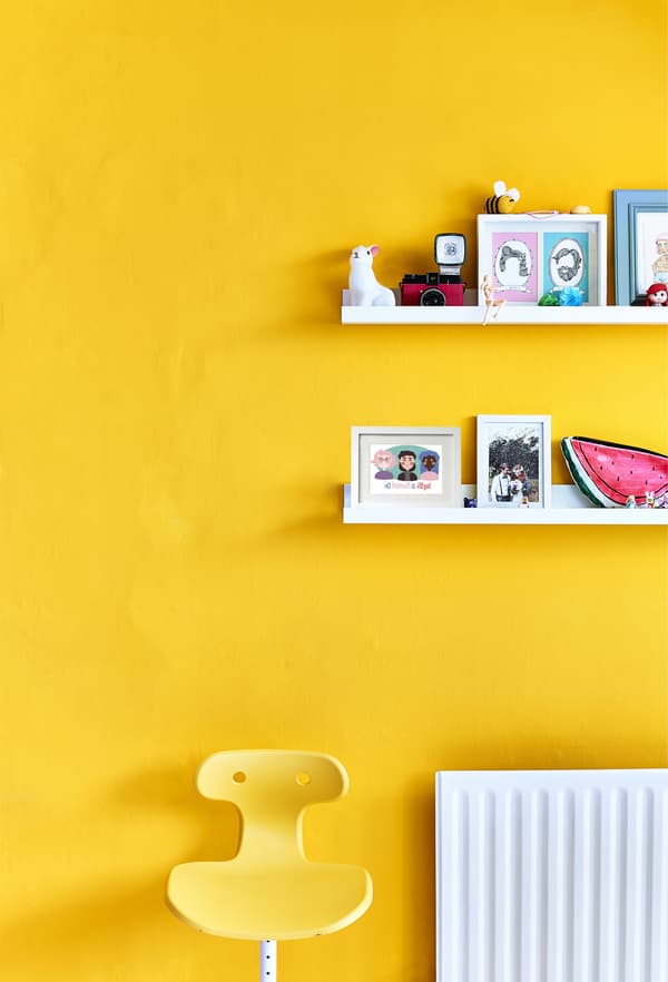 Chaise jaune sur fond de mur jaune garni de tablettes.