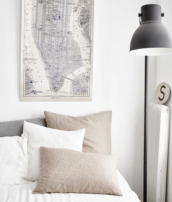 Chambre à coucher aux couleurs neutres. Gros plan sur le linge de lit, la carte affichée au mur et le lampadaire. 