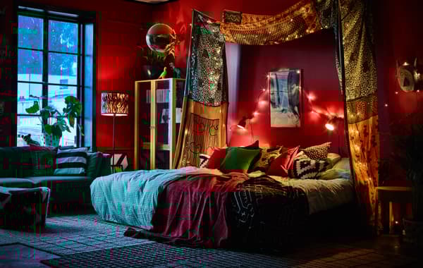 Chambre à coucher aux murs rouges en fin d’après-midi, avec une guirlande lumineuse accrochée aux murs.
