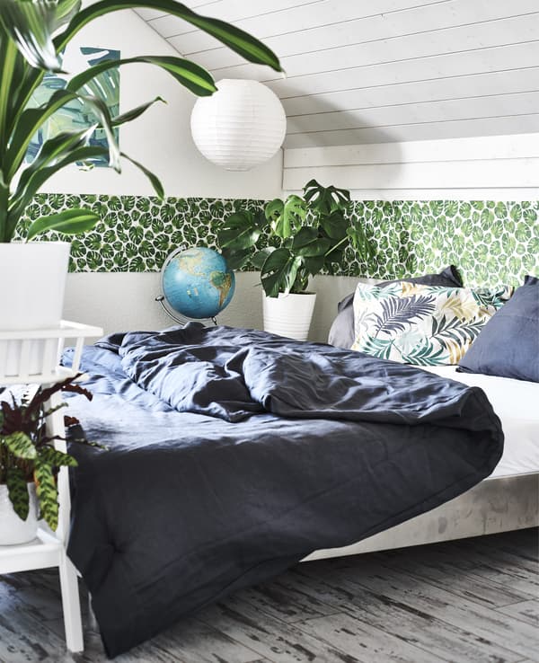 Chambre à coucher avec cache-pots, frise de feuillage vert et parure de lit foncée.
