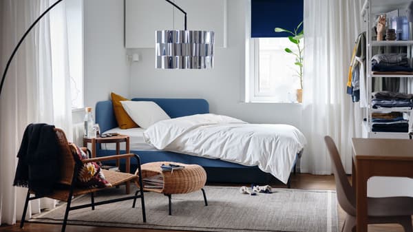 Chambre à coucher avec cadre de lit matelassé et tête de lit d’angle, housse de couette et taie d’oreiller blanches, plante en pot.