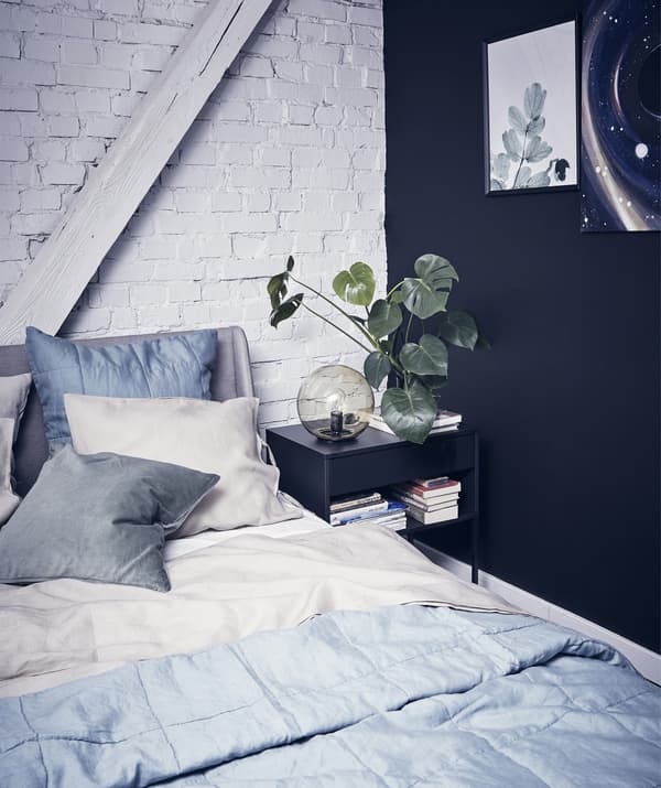 Chambre à coucher avec linge de lit gris en superposition, un mur noir et un mur en briques peint en blanc