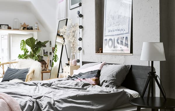 Chambre à coucher avec linge de lit gris, murs blancs et fauteuil en rotin.