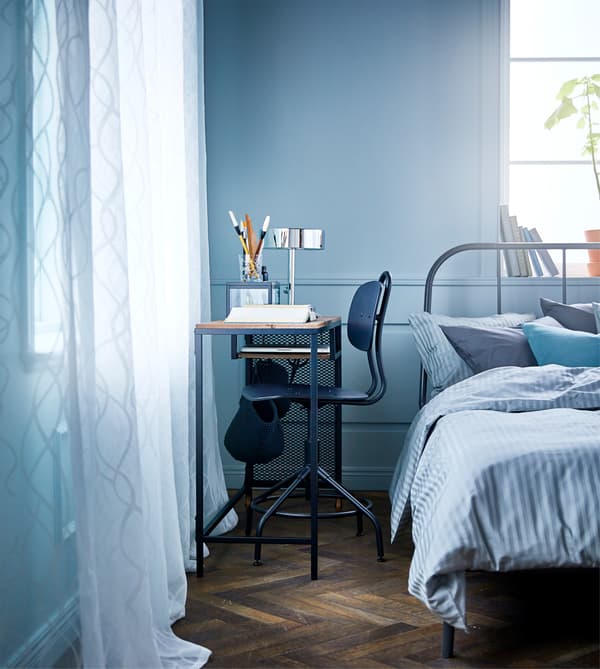 Chambre à coucher avec table pour portable sur roulettes, en métal et bois massif, et chaise pivotante, installées entre le lit et le mur
