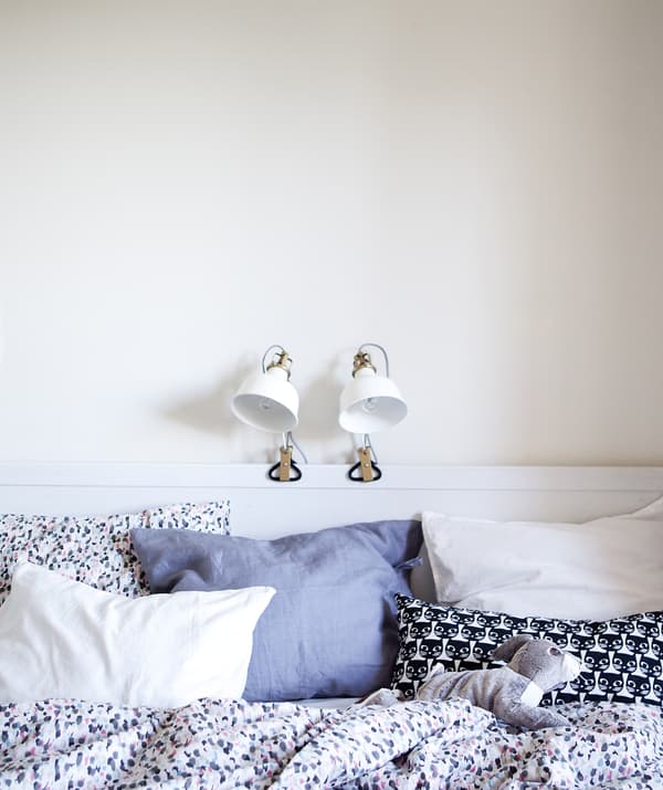 Chambre à coucher blanche avec deux lampes accrochées au cadre de lit.