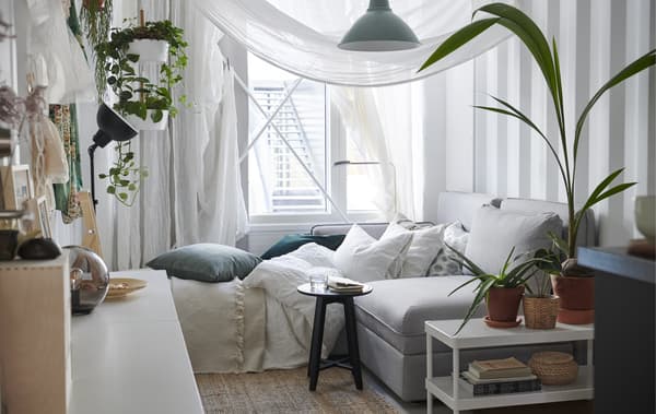 Chambre à coucher blanche avec textiles neutres, voilages autour du canapé et plantes en pot.