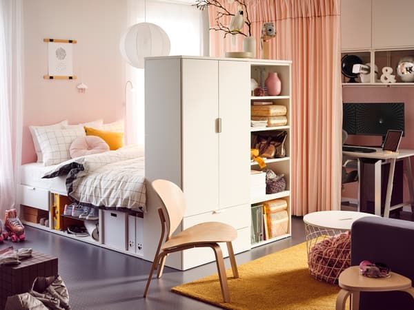 Chambre à coucher d’ado avec cadre de lit PLATSA, objets et paniers sur des tablettes à l’extrémité du lit et tapis jaune sur le sol.