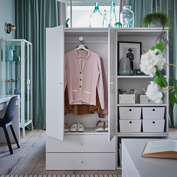 Chambre à coucher en gris/vert, avec rangements et étagères en blanc. Les portes ouvertes de la penderie dévoilent des vêtements à l'intérieur.