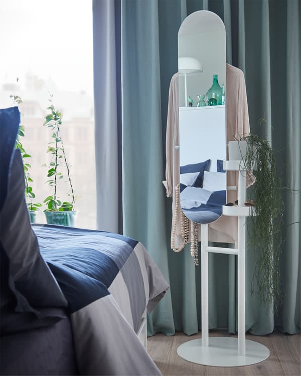 Chambre à coucher en gris/vert. Un valet blanc à miroir est posé dans un coin, près de rideaux verts.