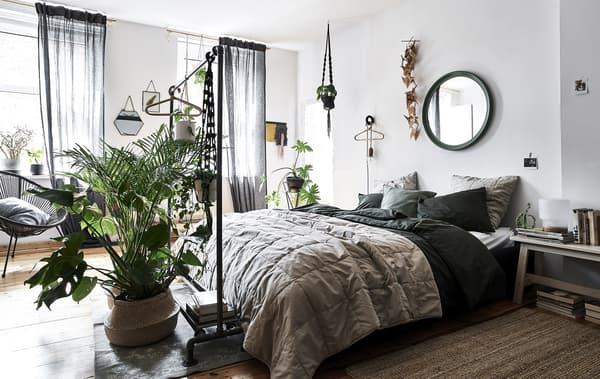 Chambre à coucher peinte en blanc, linge de lit aux teintes naturelles, et plantes dans des paniers en osier