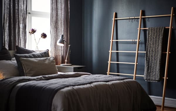 Chambre aux murs foncés avec fenêtre, lit, table de chevet et échelle porte-serviettes.