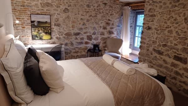 Chambre avec des murs en pierre apparente et gros plan sur un lit avec des textiles blancs et beiges