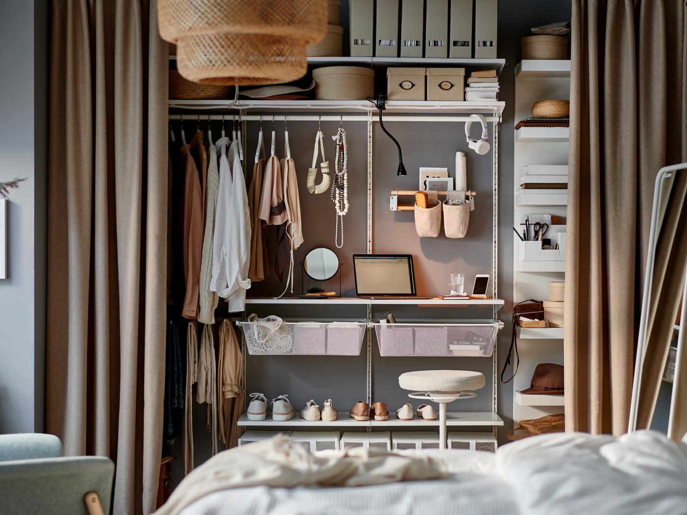 Chambre avec petit poste de travail sur quelques tablettes d’un rangement modulaire à l’intérieur d’une penderie ouverte avec des rideaux utilisés comme portes.