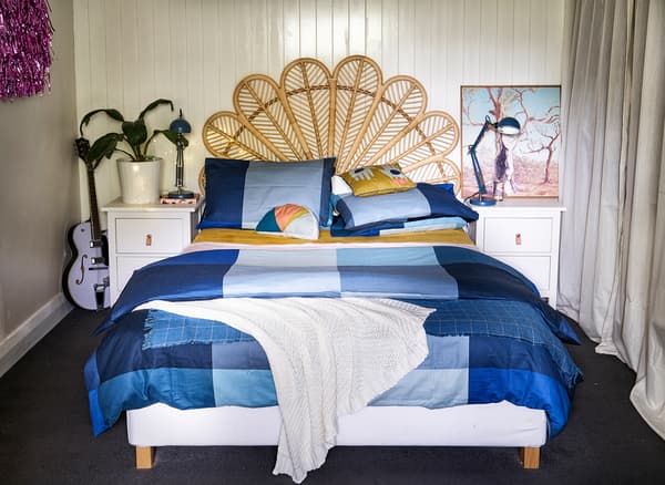 Chambre avec tête de lit en osier, linge de lit bleu et tables de chevet blanches.