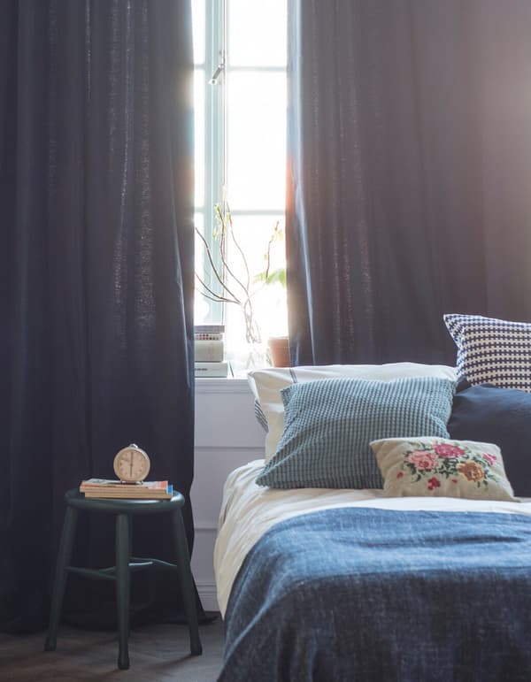 Chambre décorée avec des textiles dans des teintes de bleu et de blanc et des rideaux tombant du plafond jusqu’au sol.