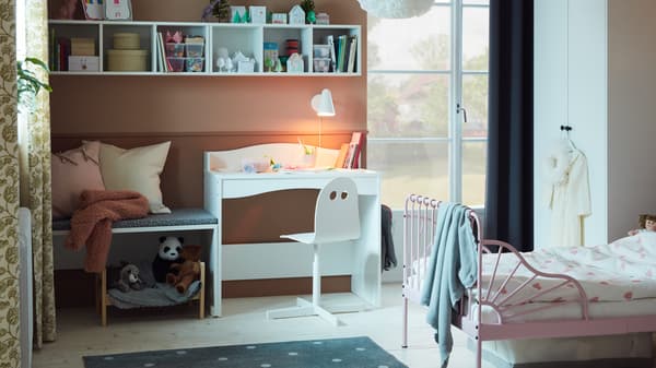 Chambre d’enfant avec cadre de lit extensible en finition rose pâle avec sommier à lattes, bureau blanc et peluches.