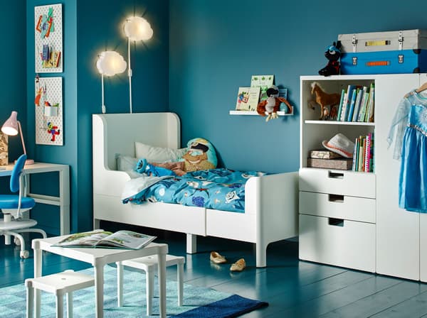 Chambre d'enfant bleue avec lit extensible, armoire, table et tabourets blancs.