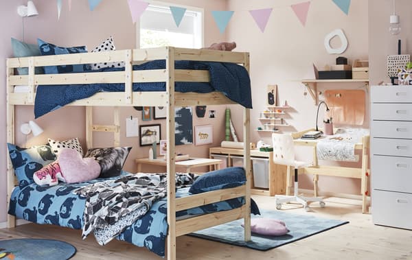 Chambre d’enfant: murs rose clair, lits superposés et linge de lit bleu, meuble de rangement et table en bois clair.