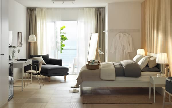 Chambre d’hôtel en blanc et bois avec lit, bureau, méridienne et vue sur la mer.