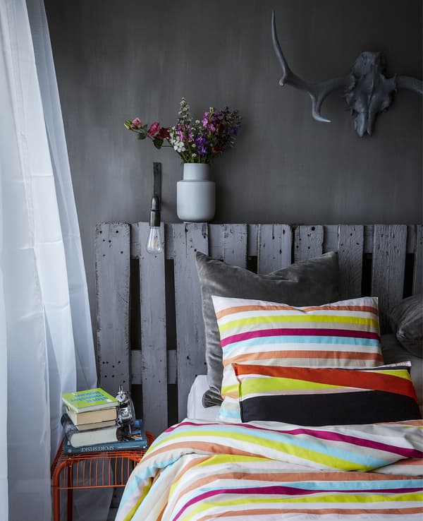 Chambre grise avec literie colorée et tabouret orange.