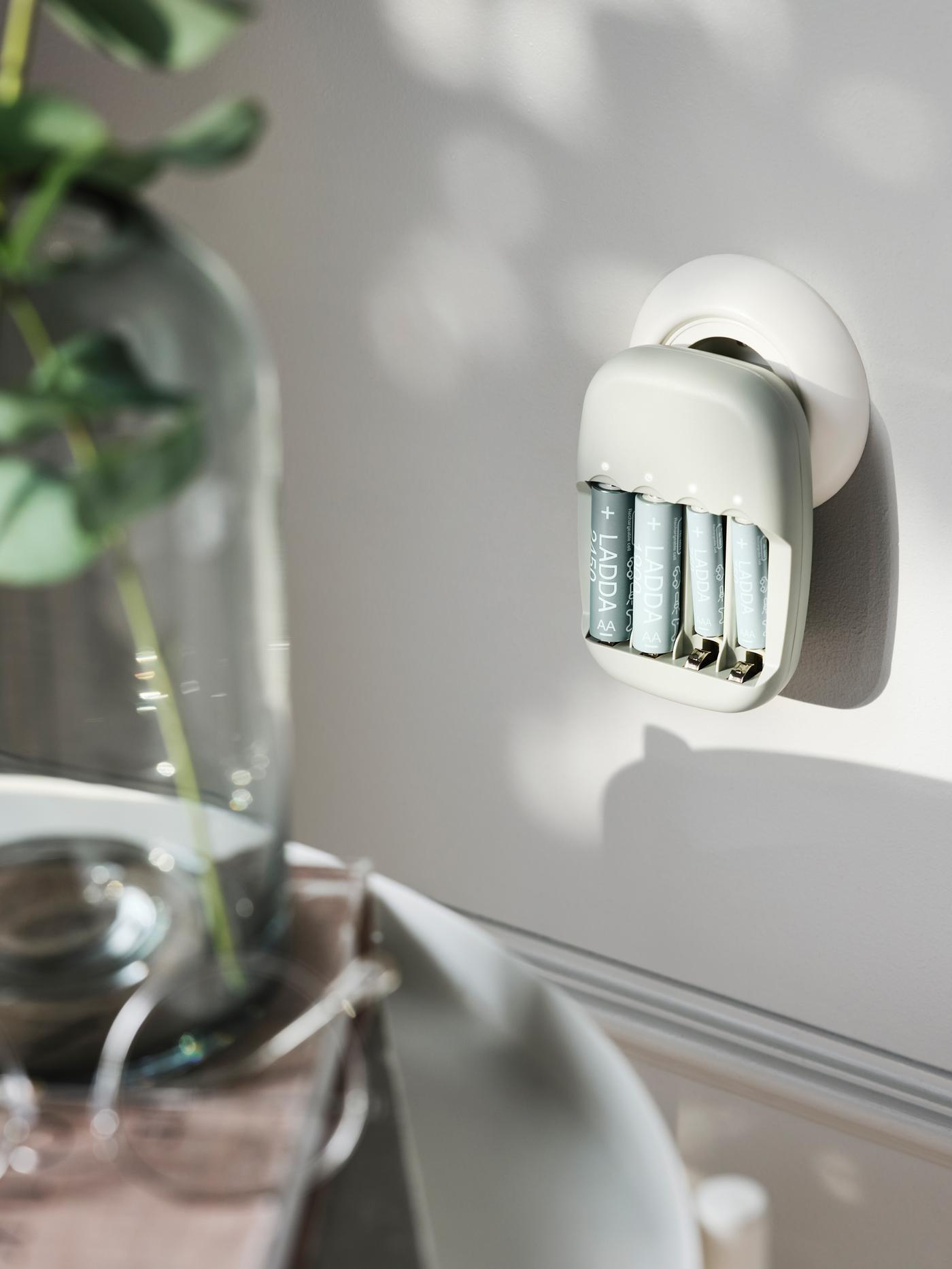 Chargeur LADDA rechargeant des piles. Il est branché sur une prise de courant ronde installée dans un mur gris clair.