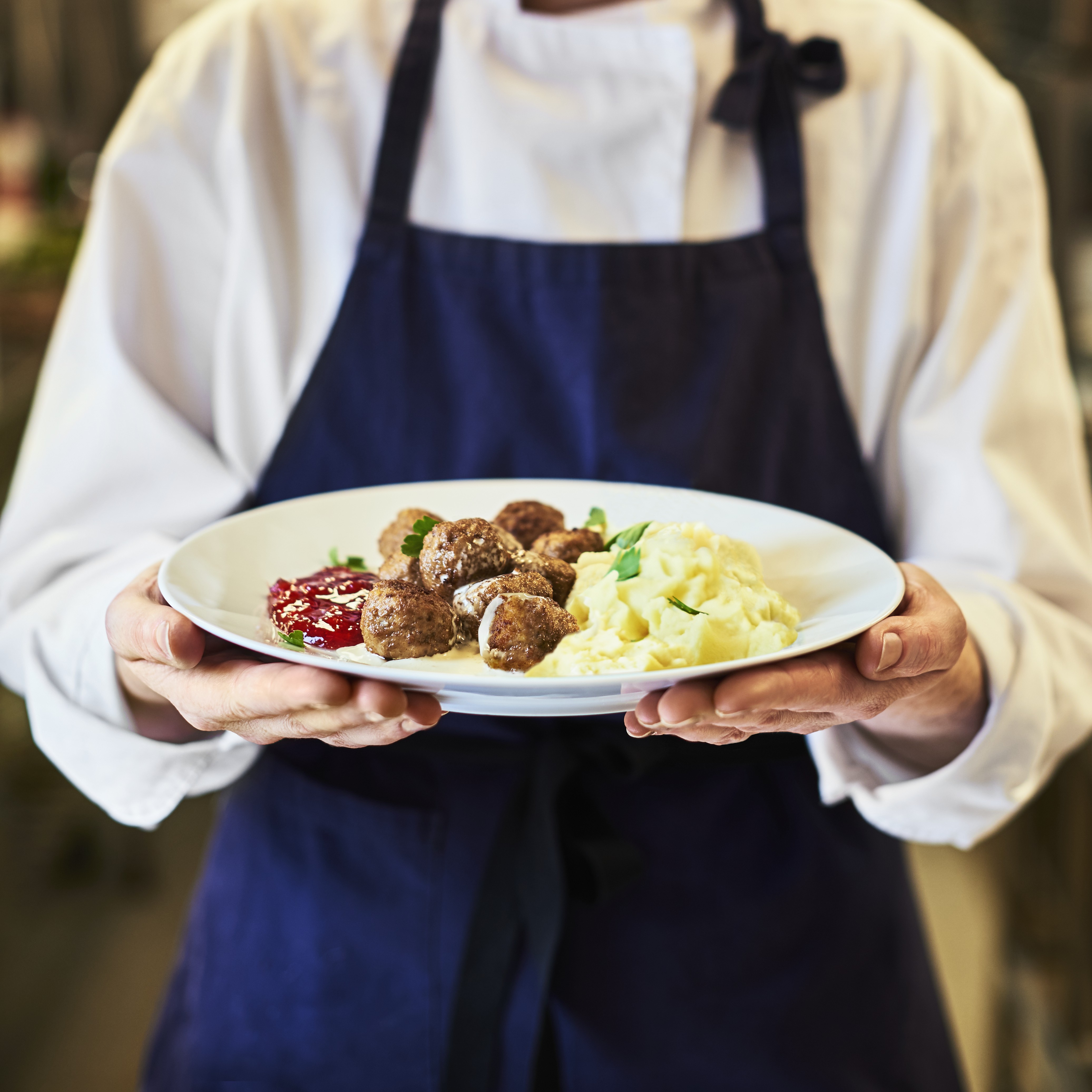 Chef mostrando un platillo de albóndigas con puré de papa y mermelada de arándanos