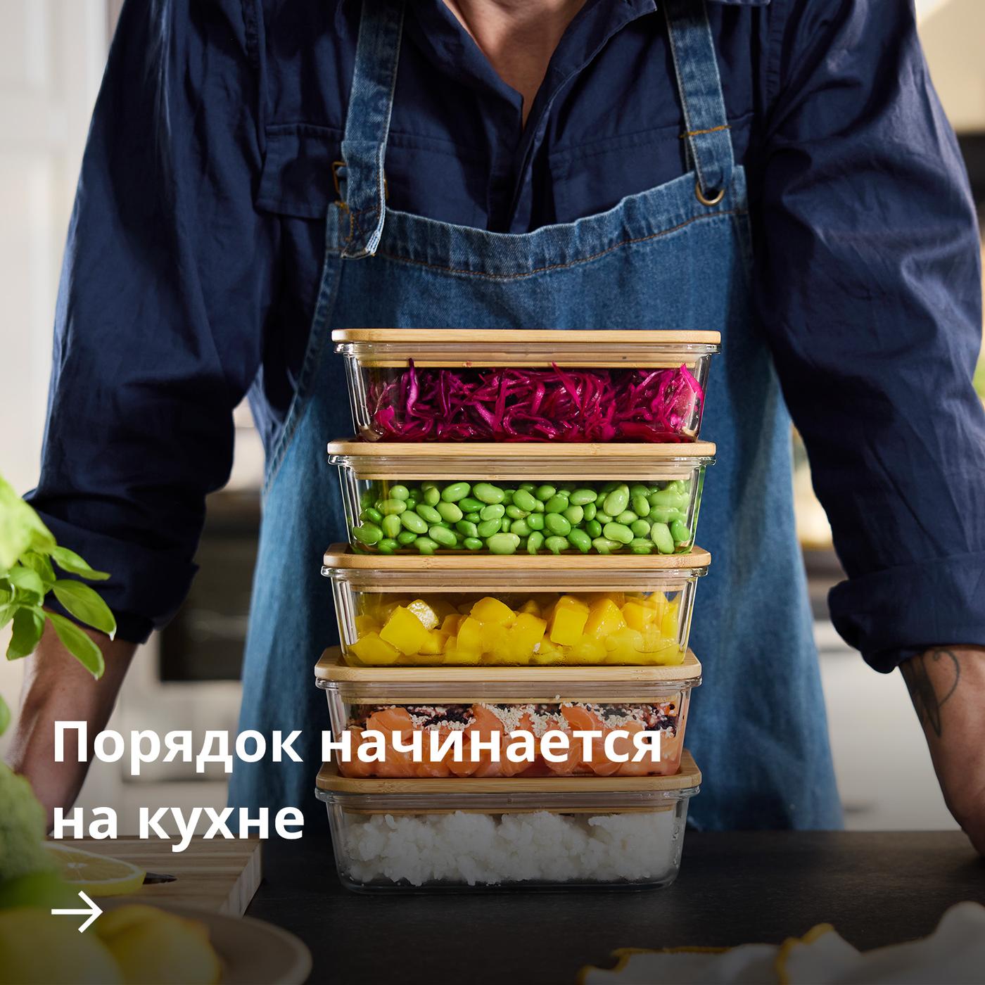 Человек стоит рядом со стопкой разноцветных контейнеров для хранения продуктов IKEA 365+, наполненных различными ингредиентами и готовыми блюдами.