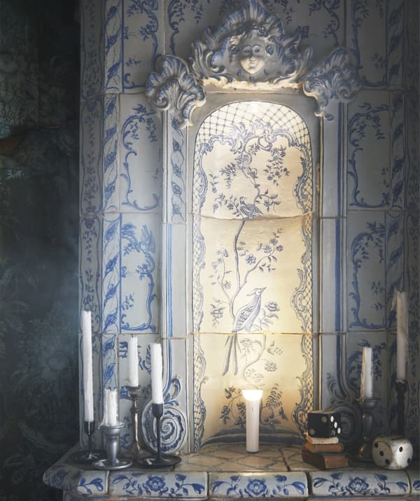 Cheminée en bleu et blanc en carreaux de Delft entourée de bougies et éclairée par une lampe torche en son centre.