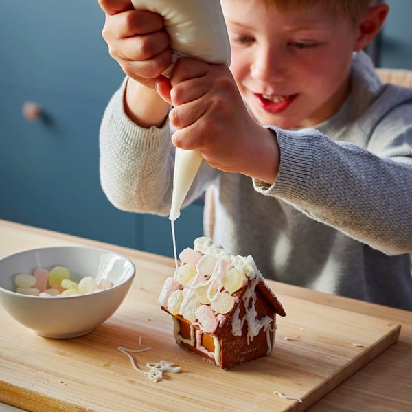 Child decorating gingerbread house with icing