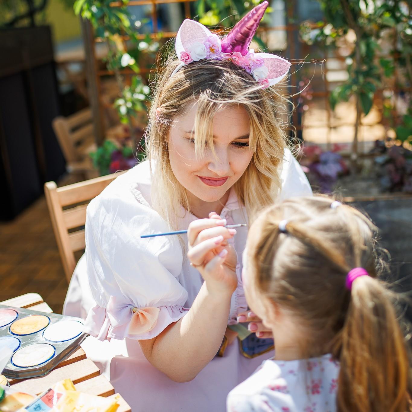 Child face painting activity, showing a person painting a design on a child’s forehead outdoors.