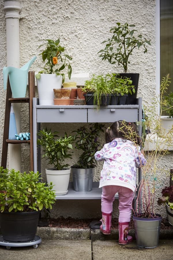 Child in pink clothes playing by outoor plants.