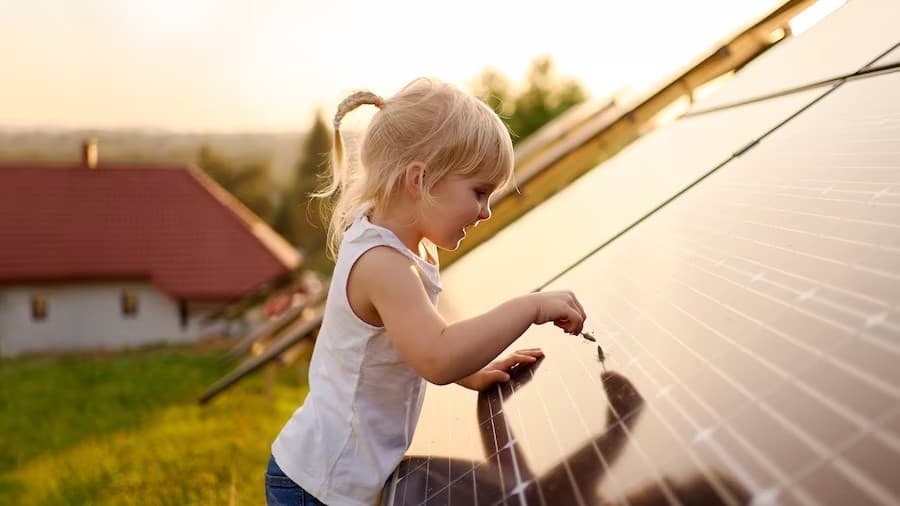 Child interacting with solar panels outdoors near a house with a red roof on a sunny day.
