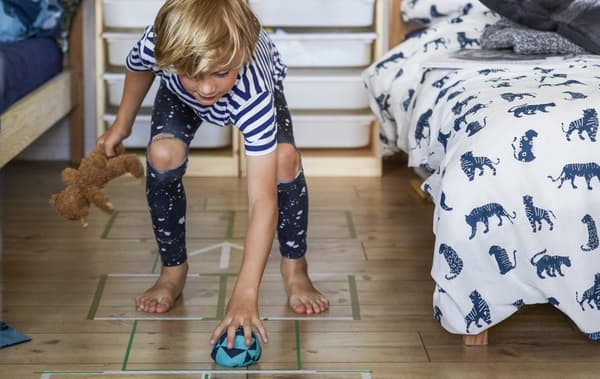 Child playing hopscotch on a wooden floor between two beds.