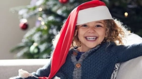 Child wearing a Santa hat sits on a couch near a decorated Christmas tree.