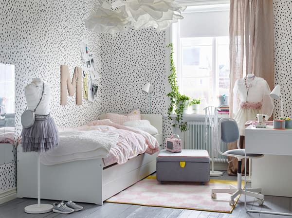 Children’s bedroom, featuring white walls with black spots and a white bed with pale pink bedding.