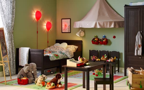 Children’s bedroom with matching wood bed, chairs, wardrobe and table. Soft toys on the floor, table set up to play shop.