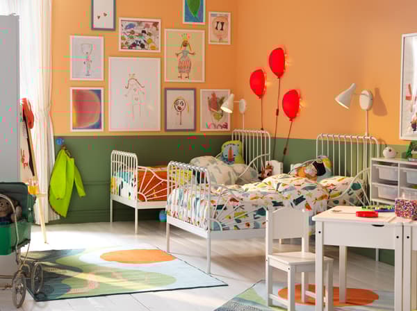 Children’s bedroom with two white, extendable beds, writing table and chair. Walls painted in green and orange.